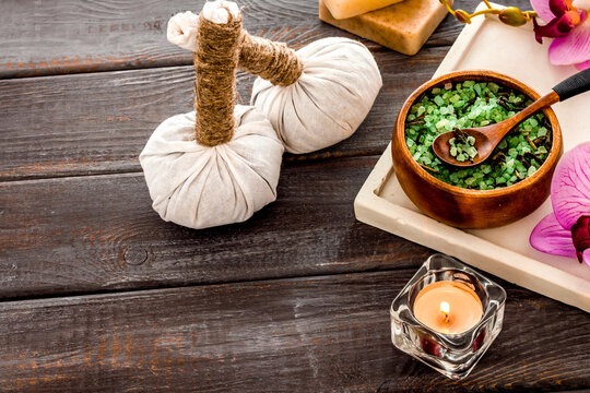 Massage thai herbal balls near spa accessories and orchids on dark wooden background copy space