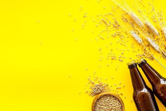 Beer ingredients. Barley near beer bottles on yellow background top view copy space