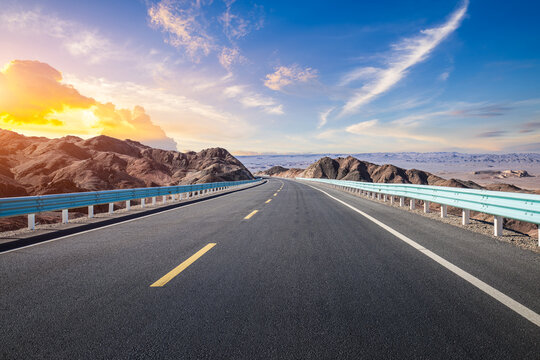 Empty asphalt road stretching through a mountainous desert landscape under a sunset sky in Qinghai, China