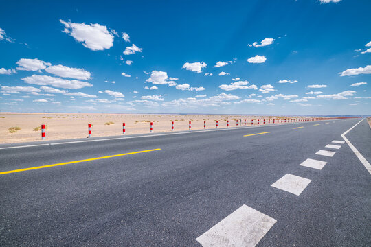 Empty asphalt highway stretching to the horizon through a desert landscape under a blue sky with clouds in Qinghai, China