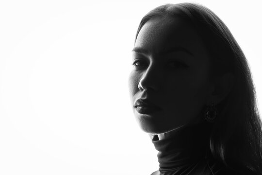 Backlit side profile of a young caucasian woman with a hoop earring against a bright high key background, a deep shadow across her face and a large empty area for text.