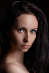 Fototapeta premium Mature caucasian brunette woman with long smooth dark hair and blue eyes on a black background in soft studio light, for haircare, keratin treatment and salon advertising.