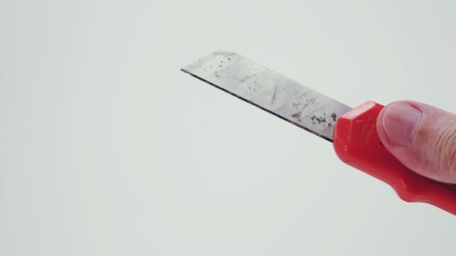 Una mano impugna un vecchio taglierino in plastica su sfondo bianco e vuoto, inquadratura ravvicinata