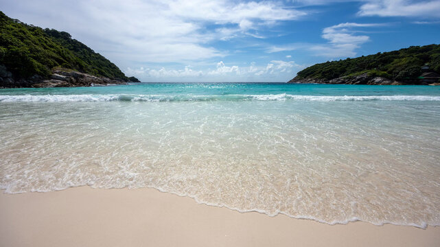 View of the pristine white sand beach and turquoise waters of Ko Racha Yai surrounded by lush green hills under a bright blue sky in Phuket, Phuket, Thailand.