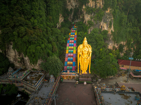 Batu Caves, Malaysia - 23 May 2024: Aerial view of the Batu Caves, featuring the giant golden statue of Lord Murugan and the vibrant rainbow-colored staircase leading into the limestone cave.