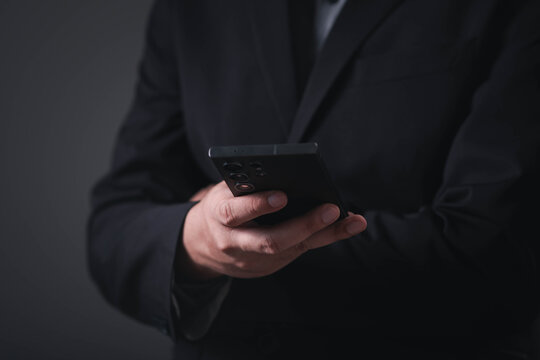 A business professional using a smartphone in a dark modern office, representing mobile communication, digital technology, online business, remote work, cybersecurity, and corporate connectivity.