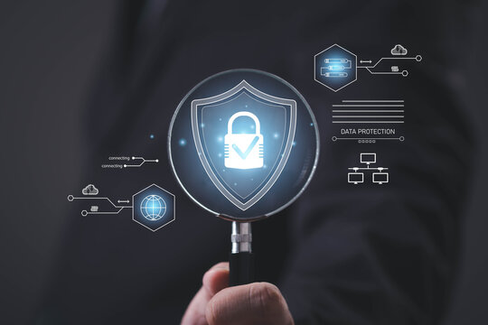 Business professional inspecting a digital security shield with a padlock through a magnifying glass, representing data protection, cybersecurity, cloud security, privacy, secure access, encryption.