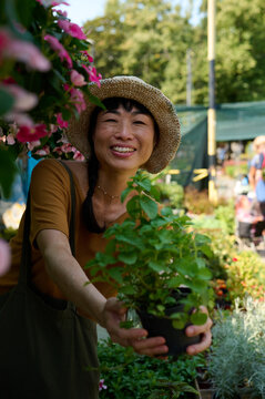 Smiling Asian Woman Buying Potted Plant at Outdoor Garden Market Wearing Straw Hat