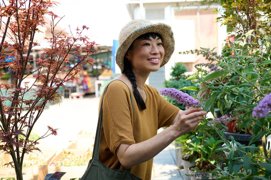 Smiling Asian Woman Shopping Plants at Outdoor Market in Summer Hat Enjoying Gardening Lifestyle