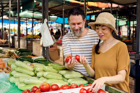 Asian Woman and Man Choosing Fresh Tomatoes at a Busy Outdoor Farmers Market Shopping Together