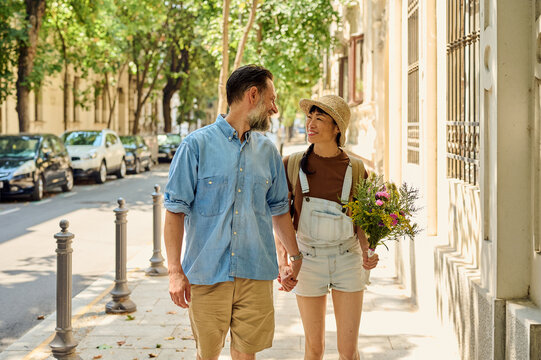 Couple Walking Hand in Hand on Sunny Urban Street With Flowers and Smiles