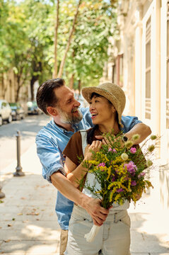 Smiling Couple Embracing on Sunny City Street With Bouquet &mdash; Romantic Summer Portrait of Asian Woman and Man