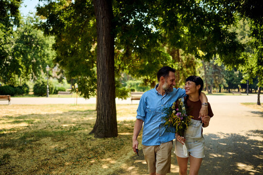 Couple Walking in Park With Wildflower Bouquet Sharing a Warm Moment on a Summer Day