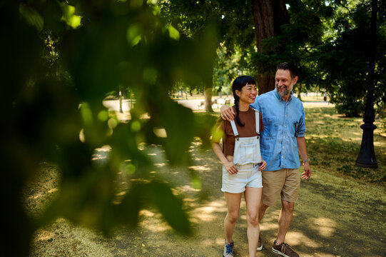 Couple Walking in Park: Asian Woman and Man Laughing While Strolling Together on a Sunny Day