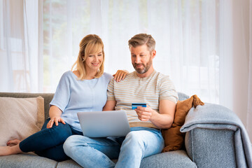 Rear view shot of a middle-aged couple using a credit card and laptop at home