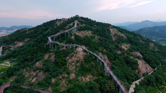 An elevated winding walkway built across a forested mountain, offering scenic views of surrounding hills and landscape.