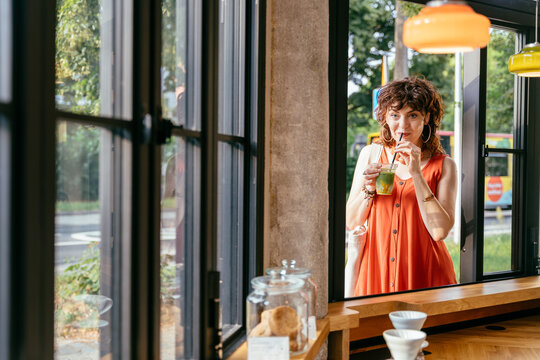 Stylish Mature Woman Drinking Iced Matcha at Modern Cafe Window