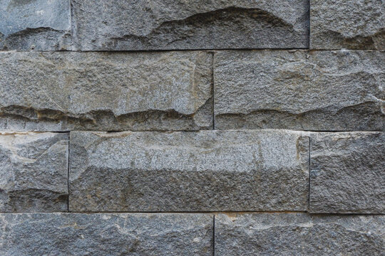 Close up of rough chiseled grey natural stone tiles covering an exterior wall.