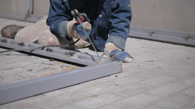 A worker in a blue uniform is welding metal beams at a construction site, showcasing a concentrated and industrious mood in a side view of the industrial work area. The scene features.