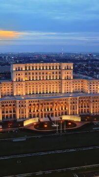 Aerial view of parliament palace in bucharest at sunset with illuminated facade and city skyline in background.