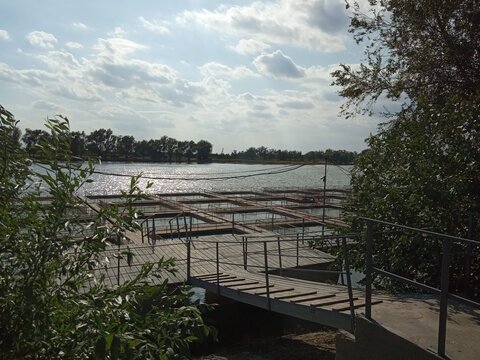 ​Fish farm cage culture on river with wooden walkways and pontoon bridges under cloudy sky at sunset