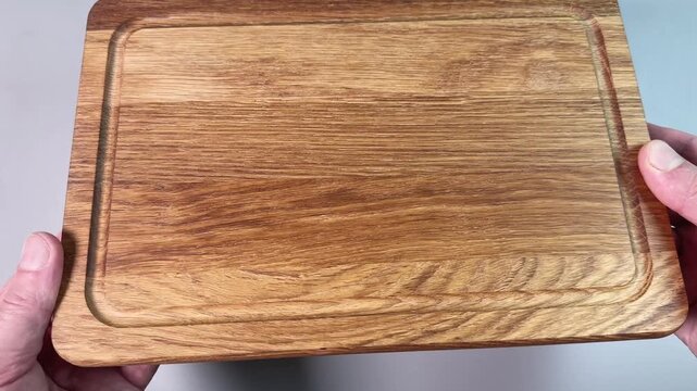 Oak cutting board with groove in hands on gray background