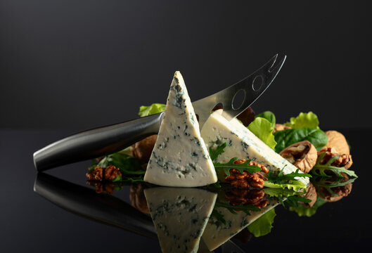 Blue cheese with knife, walnuts and fresh greens.