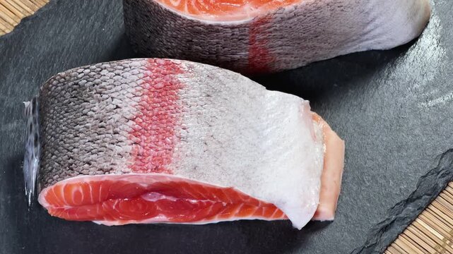 Pieces of raw rainbow trout on flat black slate plate