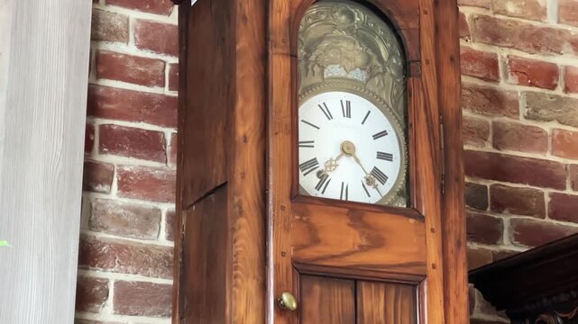 Antique longcase floor clock in wooden case against brick wall