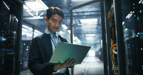 Portrait of a Data Center Engineer Using a Laptop Computer. Adult Man Looking at Camera and...
