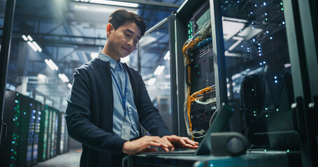 Portrait of Asian Male Data Center Specialist Using Laptop Computer on Service Cart to Run Firmware...