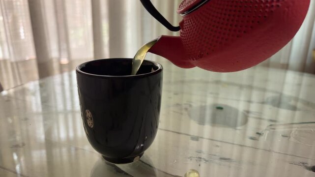 Sirviendo un poco de t&eacute; verde en una tetera de hierro