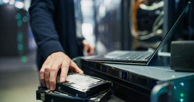 Close up of Technician Hand Selecting Hdd Hard Disk Drive From Stack Beside Laptop Computer and Server Unit on Cart During Storage Capacity Upgrade and Data Recovery Work in AI Data Center Facility