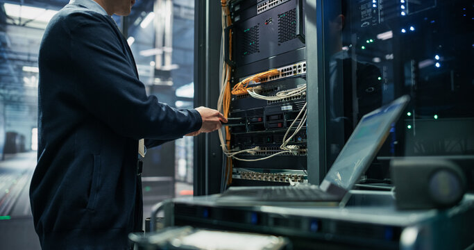 Asian Male It Technician Inserting Hard Drive Into Server Rack Unit While Working on Laptop Computer Placed on Cart for Storage Expansion and System Diagnostics in AI Cloud Data Center Facility