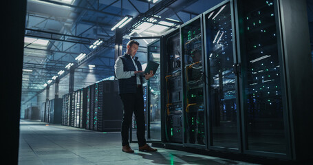 Obraz na płótnie Canvas Caucasian Male It Engineer Using Laptop Computer for System Maintenance and Hardware Troubleshooting Beside Open Server Rack Cabinet in Modern Cloud Computing and AI Data Center Warehouse