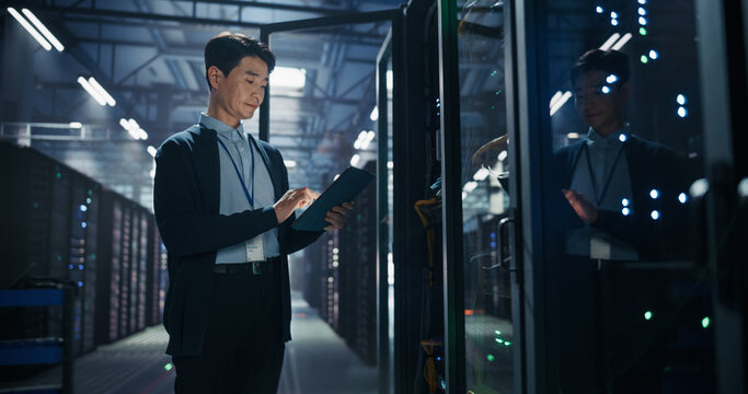 Asian Male Data Center Technician Using Tablet Computer Beside Server Rack, Performing Equipment Inspection and Remote Monitoring of AI Neural Network Hardware in Cloud Computing Facility