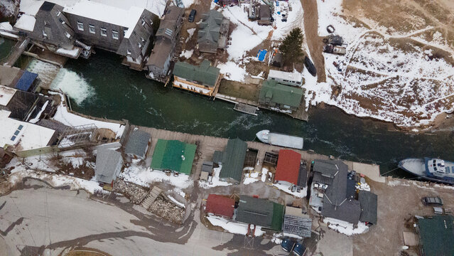 Leland, Michigan, United States - 03 March 2021: Aerial view of Historic Fishtown featuring weathered fishing shanties, snow-covered rooftops, and the river flowing into Lake Michigan.