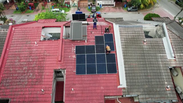 Aerial view of unrecognizable workers installing solar photovoltaic or PV panels onto red rooftop of residential house in Malaysia