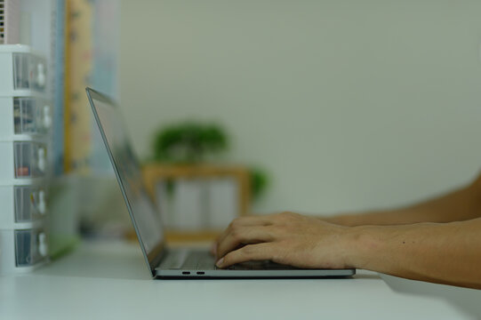 Modern person typing on laptop computer at work desk in home office setting
