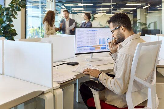 Manager analyst businessman reviews finance data analytics. He studies spreadsheet charts on a computer monitor, preparing reporting in a bright open office. Clear business data analytics concept.
