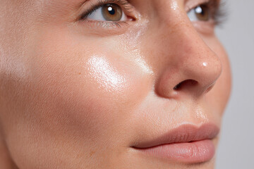 Naklejka premium Glowing dewy skin close up with natural sheen and soft texture highlighting cheek, nose and lips, capturing radiant complexion and fresh makeup look