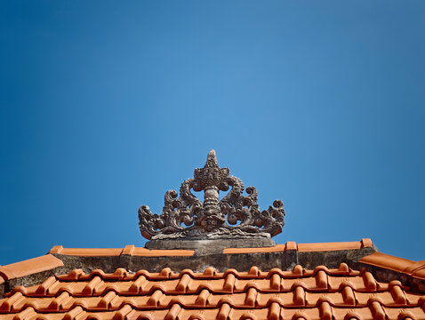 Ornate Balinese Stone Crown Carving on Clay Tile Roof Against Clear Blue Sky