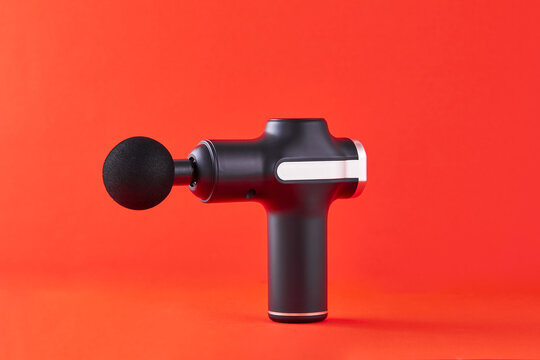 Massage gun machine or electric stimulator for massaging on orange background. Post-workout recovery tool for muscle physical therapy.