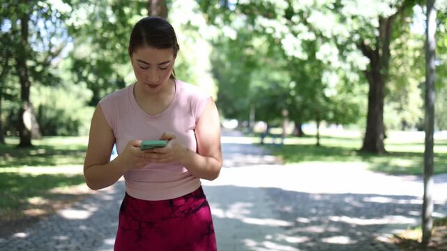 Young woman cannot resist scrolling social media even during rollerblading workout in the park checking her smartphone instead of focusing on active outdoor fitness training