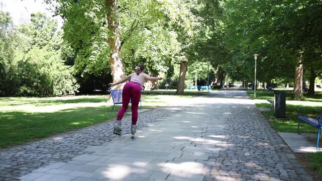 Young woman glides on one inline skate through a sunny park extending one leg behind while practicing balance coordination and control during active rollerblading session