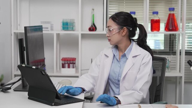 An Asian female scientist wearing a lab coat, safety goggles, and gloves is examining a raw meat sample under a microscope and recording research findings in a modern food safety laboratory.