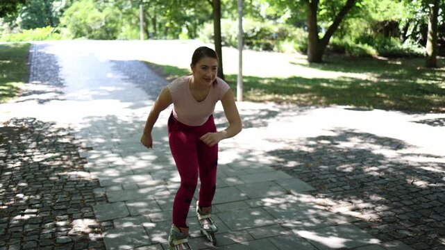 Young woman practices skating backward on inline skates in a sunny park smiling through awkward attempts while learning balance coordination and control as a beginner