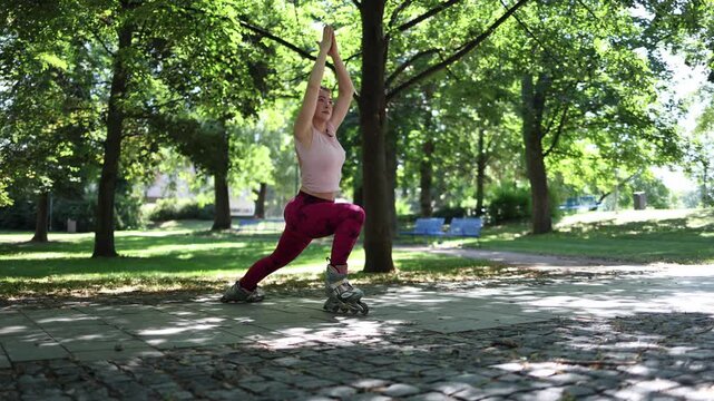 Woman mixes yoga with roller skating in a sunny park holding a deep lunge on inline skates and turning a serene wellness routine into a playful balance challenge outdoors