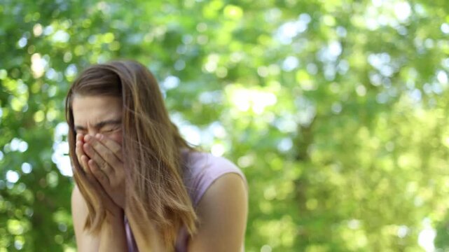 Woman with pollen allergy suddenly sneezes into her hands during a summer walk in green park as seasonal symptoms interrupt outdoor activity and cause intense discomforts