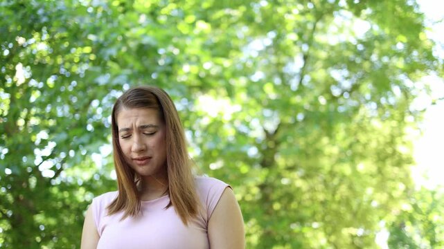 Allergic woman suffers from seasonal pollen allergy outdoors closing her eyes in discomfort as unpleasant symptoms interrupt her relaxing summer walk through a green park